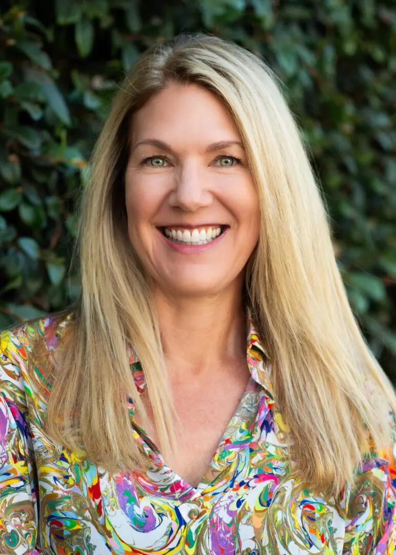 A woman with long blonde hair wearing a colorful shirt.