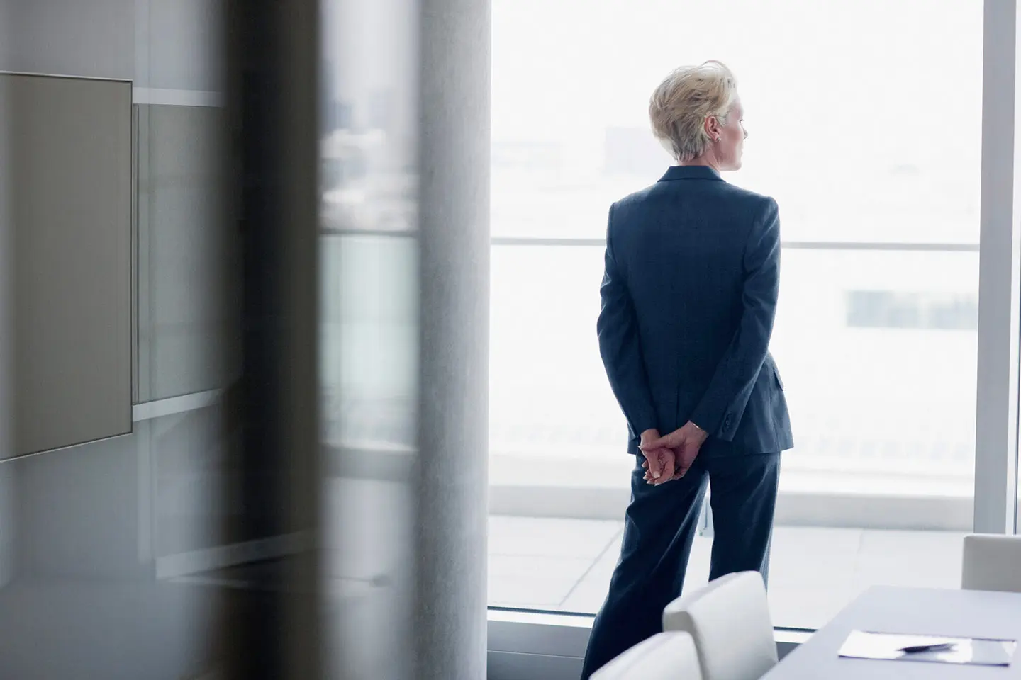 A woman in a suit standing next to a window.